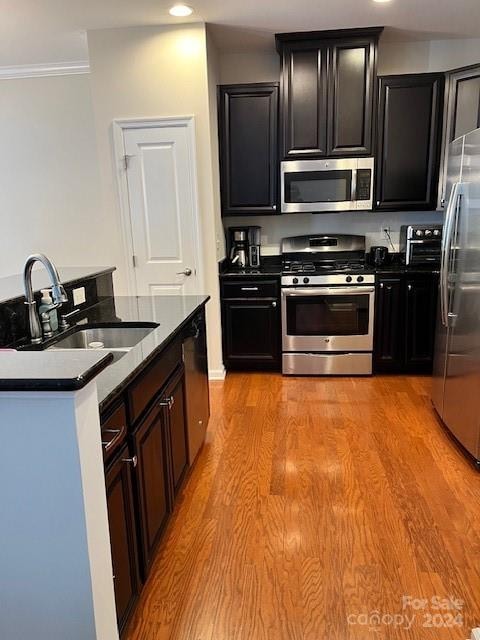 kitchen featuring appliances with stainless steel finishes, ornamental molding, sink, and light hardwood / wood-style flooring