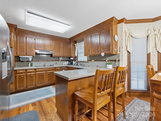 kitchen with sink, light hardwood / wood-style flooring, kitchen peninsula, a textured ceiling, and black electric cooktop