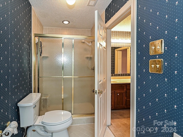 bathroom featuring vanity, tile patterned flooring, toilet, walk in shower, and a textured ceiling