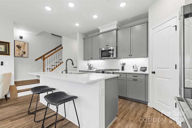 kitchen featuring appliances with stainless steel finishes, a kitchen breakfast bar, an island with sink, wood-type flooring, and sink