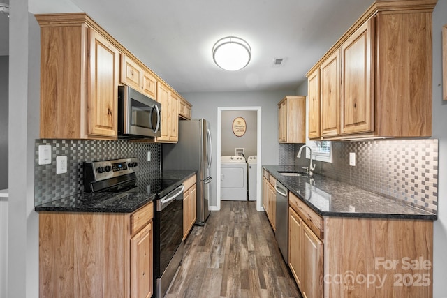 kitchen with washing machine and clothes dryer, sink, stainless steel appliances, dark hardwood / wood-style floors, and dark stone counters