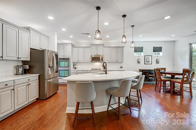 kitchen with wood-type flooring, stainless steel appliances, tasteful backsplash, pendant lighting, and a center island with sink