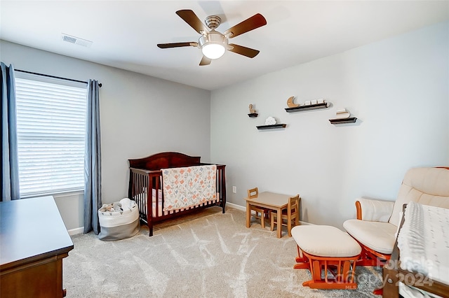 bedroom with ceiling fan, a nursery area, and light colored carpet