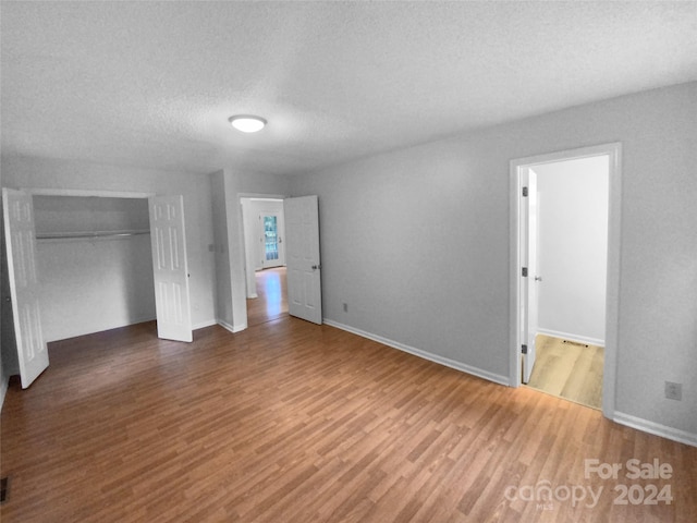 unfurnished bedroom with a textured ceiling, a closet, and hardwood / wood-style flooring