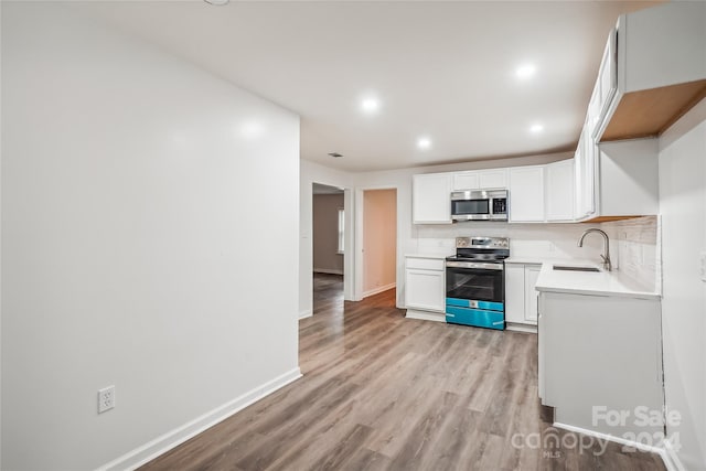 kitchen featuring tasteful backsplash, sink, white cabinetry, light hardwood / wood-style flooring, and stainless steel appliances