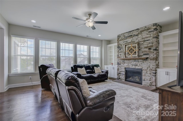 living room with ceiling fan, dark hardwood / wood-style flooring, a stone fireplace, and built in features