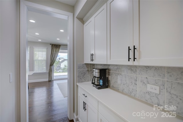 bar featuring dark hardwood / wood-style flooring, backsplash, and white cabinetry