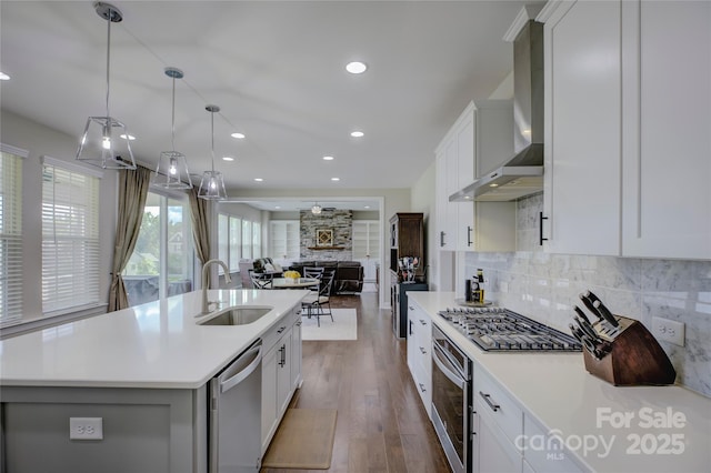 kitchen featuring a kitchen island with sink, wall chimney range hood, sink, decorative backsplash, and appliances with stainless steel finishes