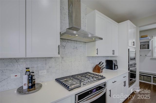 kitchen with white cabinets, wall chimney exhaust hood, appliances with stainless steel finishes, tasteful backsplash, and dark hardwood / wood-style flooring