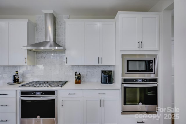 kitchen featuring white cabinets, appliances with stainless steel finishes, tasteful backsplash, and wall chimney range hood