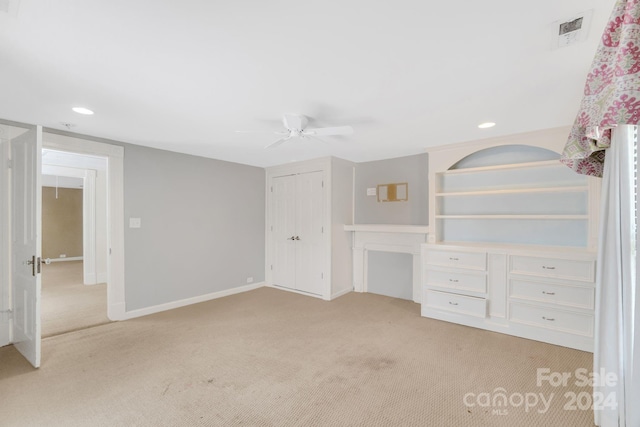 unfurnished bedroom featuring ceiling fan, light carpet, and built in desk