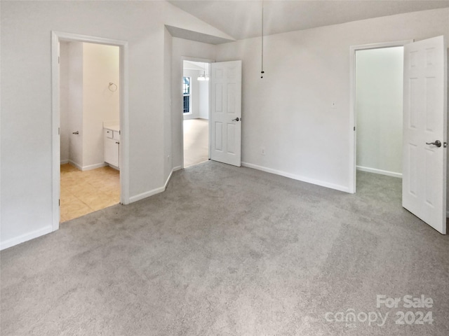 unfurnished bedroom featuring connected bathroom, vaulted ceiling, and light carpet