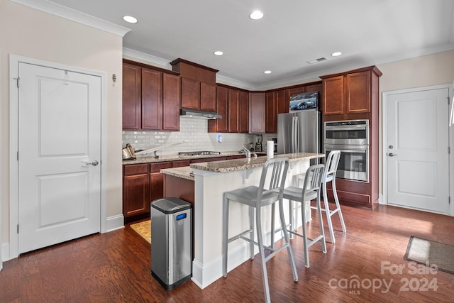 kitchen featuring dark wood-type flooring, a kitchen breakfast bar, stainless steel appliances, a center island with sink, and light stone countertops