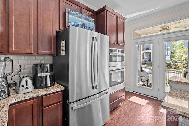 kitchen featuring appliances with stainless steel finishes, decorative backsplash, dark wood-type flooring, light stone countertops, and crown molding