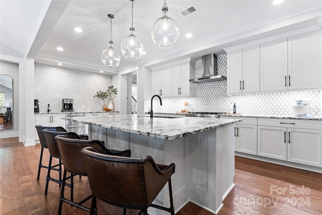 kitchen featuring a large island with sink, sink, decorative backsplash, and wall chimney range hood