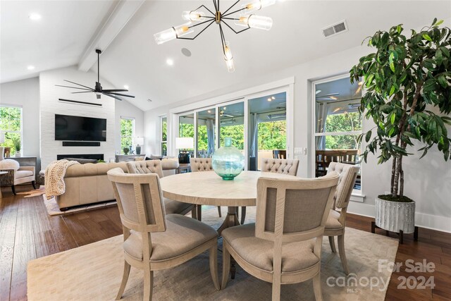 dining room with dark wood-type flooring, vaulted ceiling with beams, a fireplace, and ceiling fan with notable chandelier