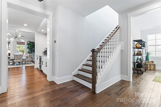 staircase with an inviting chandelier, wood-type flooring, and a healthy amount of sunlight