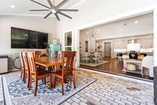 dining room with high vaulted ceiling, ceiling fan with notable chandelier, and hardwood / wood-style floors