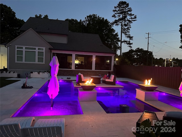 pool at dusk with an outdoor fire pit and a patio area