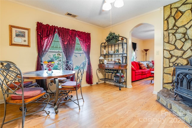 dining room featuring a wood stove, ceiling fan, crown molding, hardwood / wood-style floors, and a textured ceiling