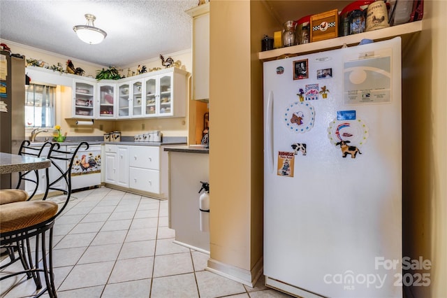 kitchen with ornamental molding, a textured ceiling, light tile patterned floors, white fridge, and white cabinetry