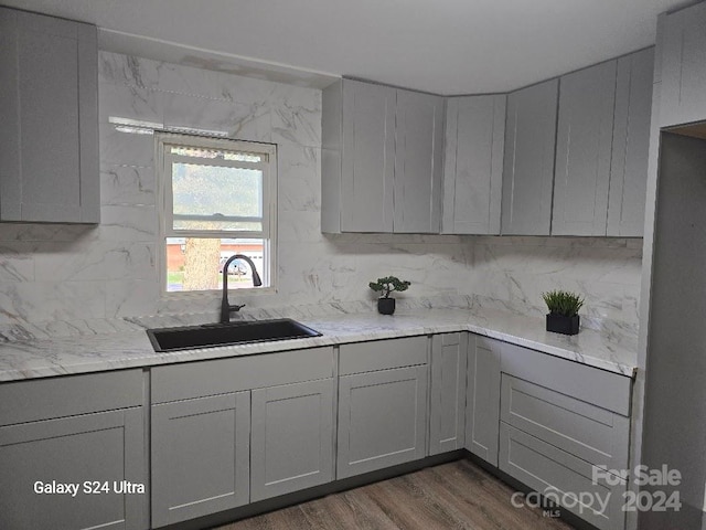 kitchen with light stone counters, sink, tasteful backsplash, gray cabinetry, and dark hardwood / wood-style flooring