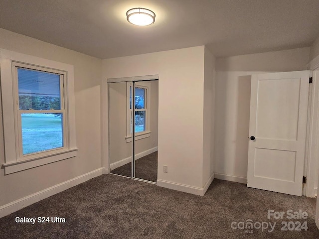 unfurnished bedroom with dark carpet and a closet