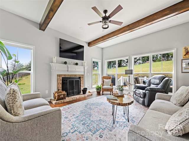 living room featuring beam ceiling, wood-type flooring, ceiling fan, and a brick fireplace