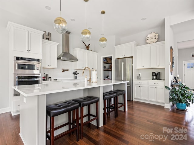 kitchen featuring white cabinetry, appliances with stainless steel finishes, a kitchen breakfast bar, decorative light fixtures, and wall chimney range hood