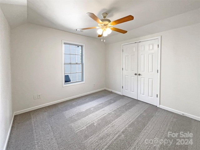 unfurnished bedroom featuring dark carpet, a closet, vaulted ceiling, and ceiling fan