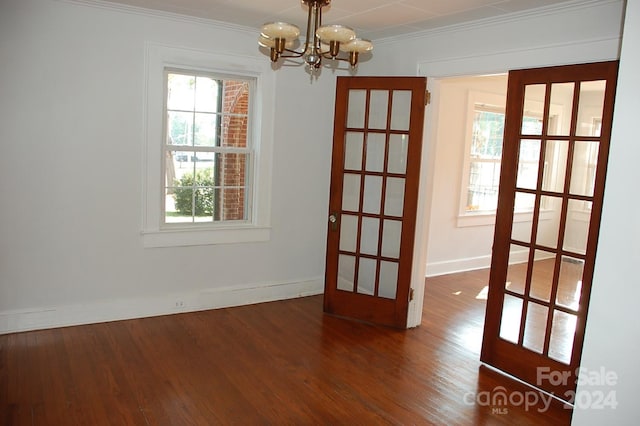 spare room with french doors, ornamental molding, an inviting chandelier, and dark wood-type flooring