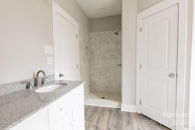 bathroom with hardwood / wood-style flooring, vanity, and a tile shower