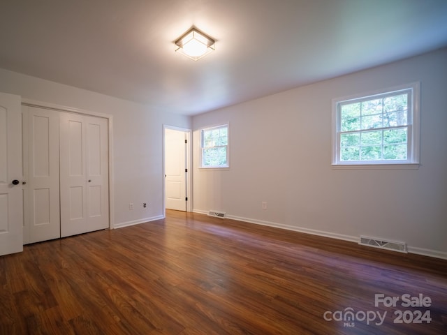 unfurnished bedroom with dark wood-type flooring, multiple windows, and a closet