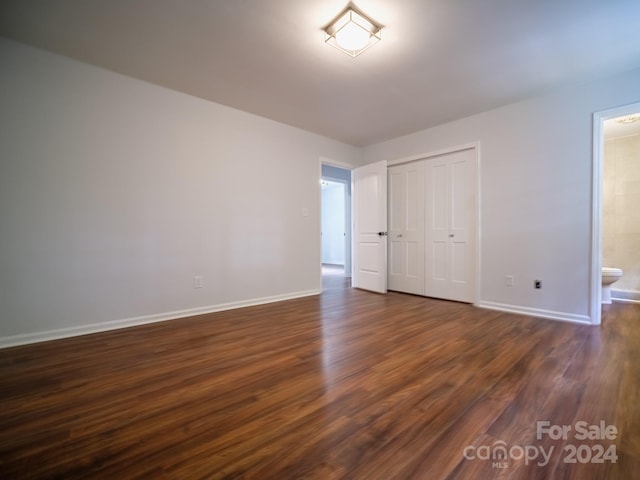 unfurnished bedroom with ensuite bathroom, a closet, and dark hardwood / wood-style flooring