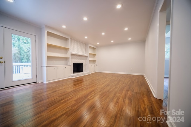 unfurnished living room featuring hardwood / wood-style flooring, a brick fireplace, built in features, crown molding, and french doors