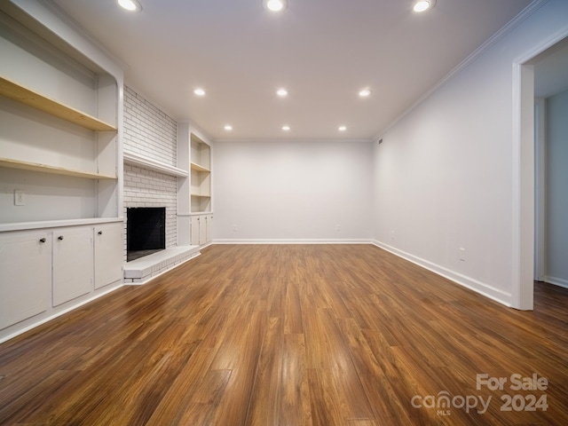 unfurnished living room featuring crown molding, hardwood / wood-style flooring, built in shelves, and a brick fireplace