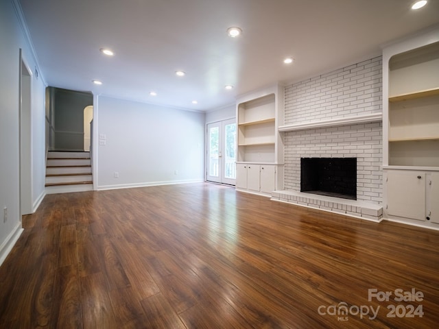 unfurnished living room featuring dark wood-type flooring, crown molding, and a brick fireplace