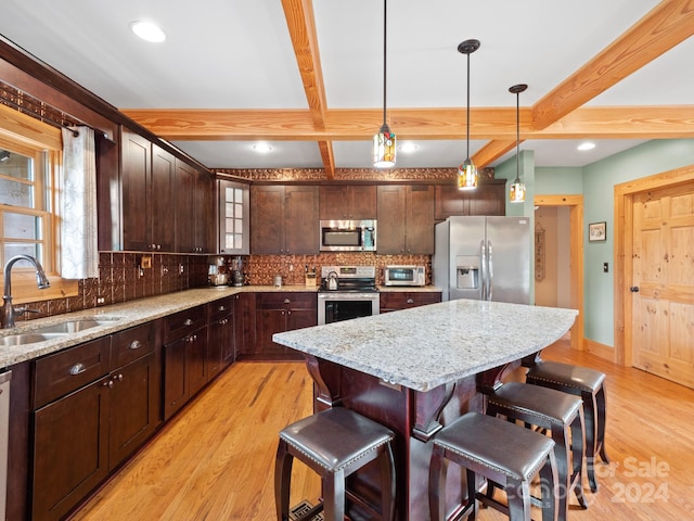 kitchen featuring a center island, beamed ceiling, hanging light fixtures, light hardwood / wood-style flooring, and stainless steel appliances