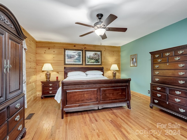 bedroom with wood walls, ceiling fan, and light hardwood / wood-style flooring