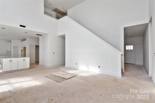 unfurnished living room with visible vents, a towering ceiling, and baseboards