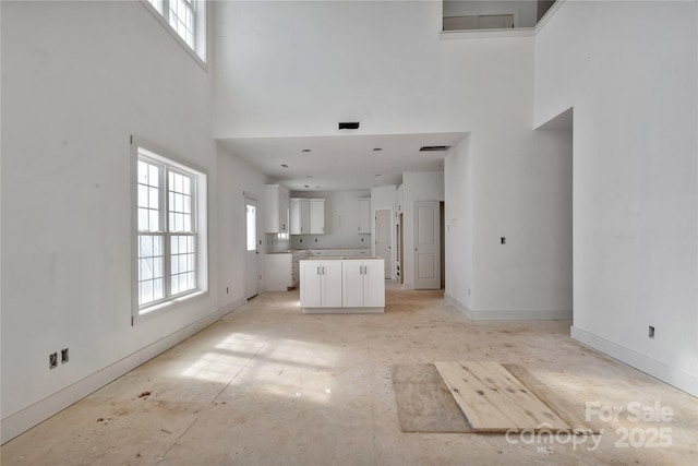 unfurnished living room with visible vents, plenty of natural light, a towering ceiling, and baseboards