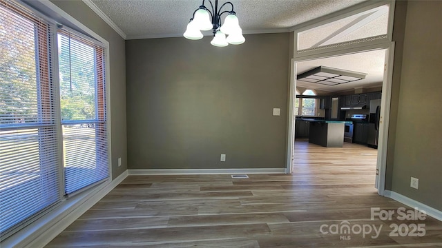 unfurnished dining area with an inviting chandelier, ornamental molding, wood-type flooring, and a textured ceiling