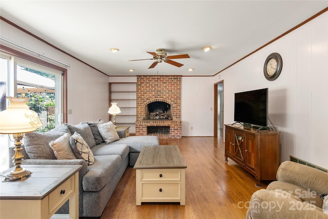 living room with crown molding, ceiling fan, a brick fireplace, and light hardwood / wood-style flooring