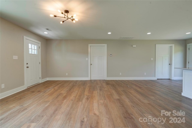 unfurnished living room featuring an inviting chandelier and light hardwood / wood-style flooring