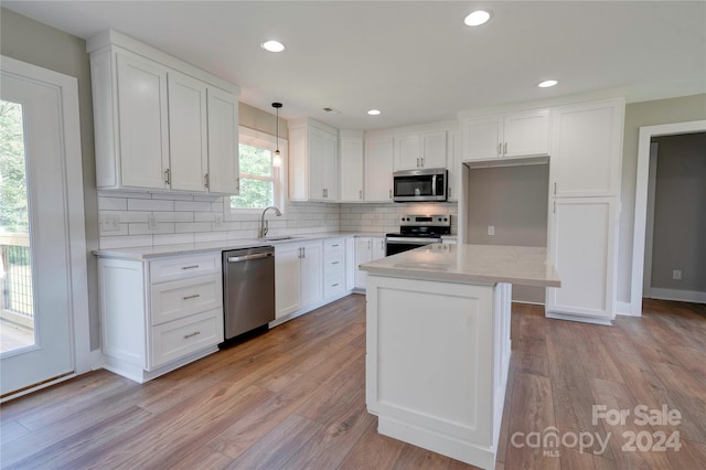 kitchen with appliances with stainless steel finishes, light hardwood / wood-style floors, white cabinetry, and decorative light fixtures