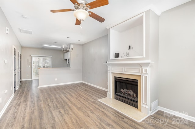 unfurnished living room with ceiling fan with notable chandelier and hardwood / wood-style flooring