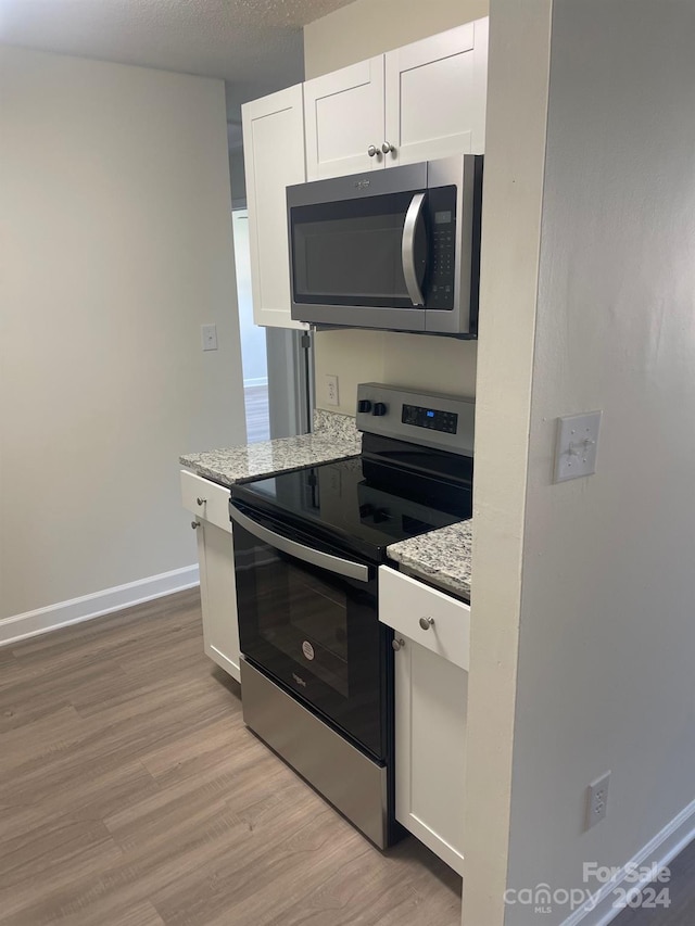 kitchen with light stone counters, a textured ceiling, white cabinetry, light hardwood / wood-style flooring, and appliances with stainless steel finishes