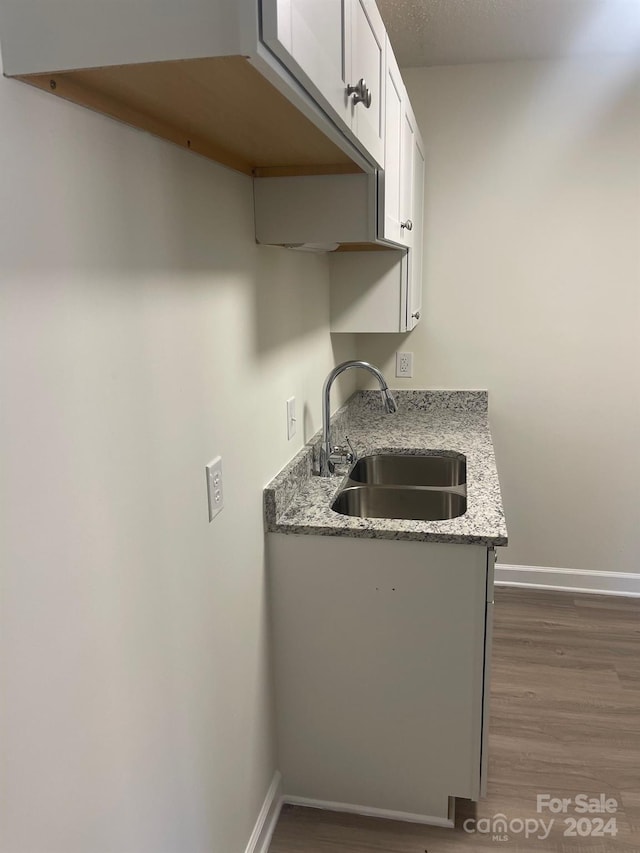 kitchen featuring dark hardwood / wood-style flooring, white cabinets, light stone counters, and sink