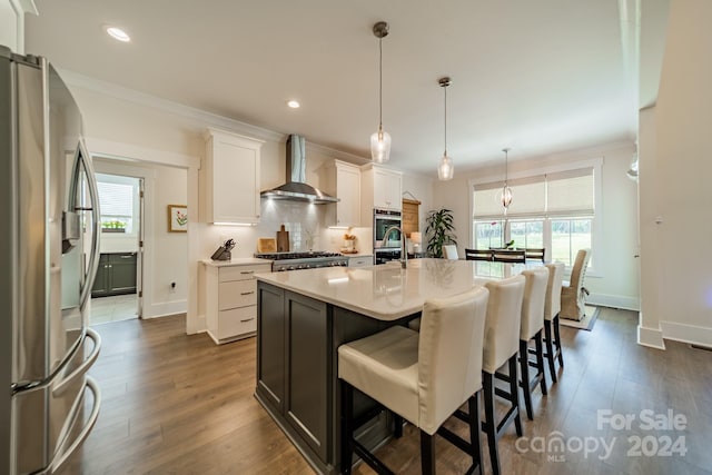 kitchen featuring wall chimney exhaust hood, a wealth of natural light, stainless steel appliances, and white cabinets