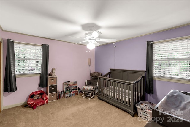 bedroom featuring a nursery area, ceiling fan, ornamental molding, and carpet floors